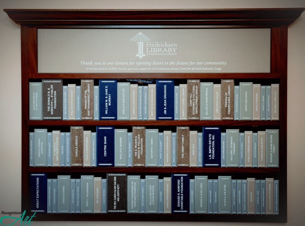 Donor wall made to look like a bookshelf with different sized book spines made of Corian engraved with donor names.