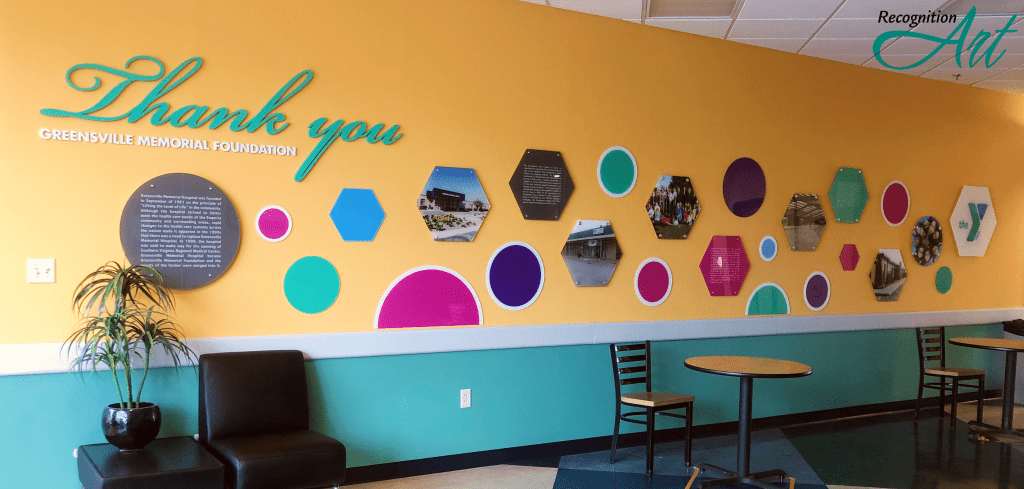 A donor wall made of pink, blue, green and purple acrylic circles and hexagons describing the journey of the Emporia-Greensville YMCA