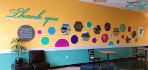 A donor wall made of pink, blue, green and purple acrylic circles and hexagons describing the journey of the Emporia-Greensville YMCA
