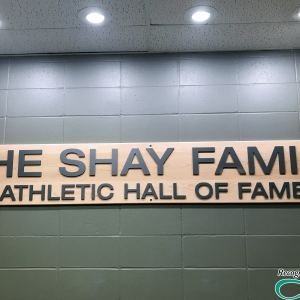 Metal letters that spell out The Shay Family Athletic Hall of Fame secured to wood backer on concrete wall