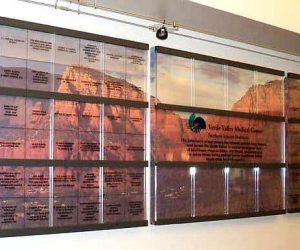 Large three-piece photo backer of a beautiful red/orange mountain scape. Small square individual clear pieces of acrylic are mounted in front with donor names that are held in separate silver frames that comprise of the donor recognition wall